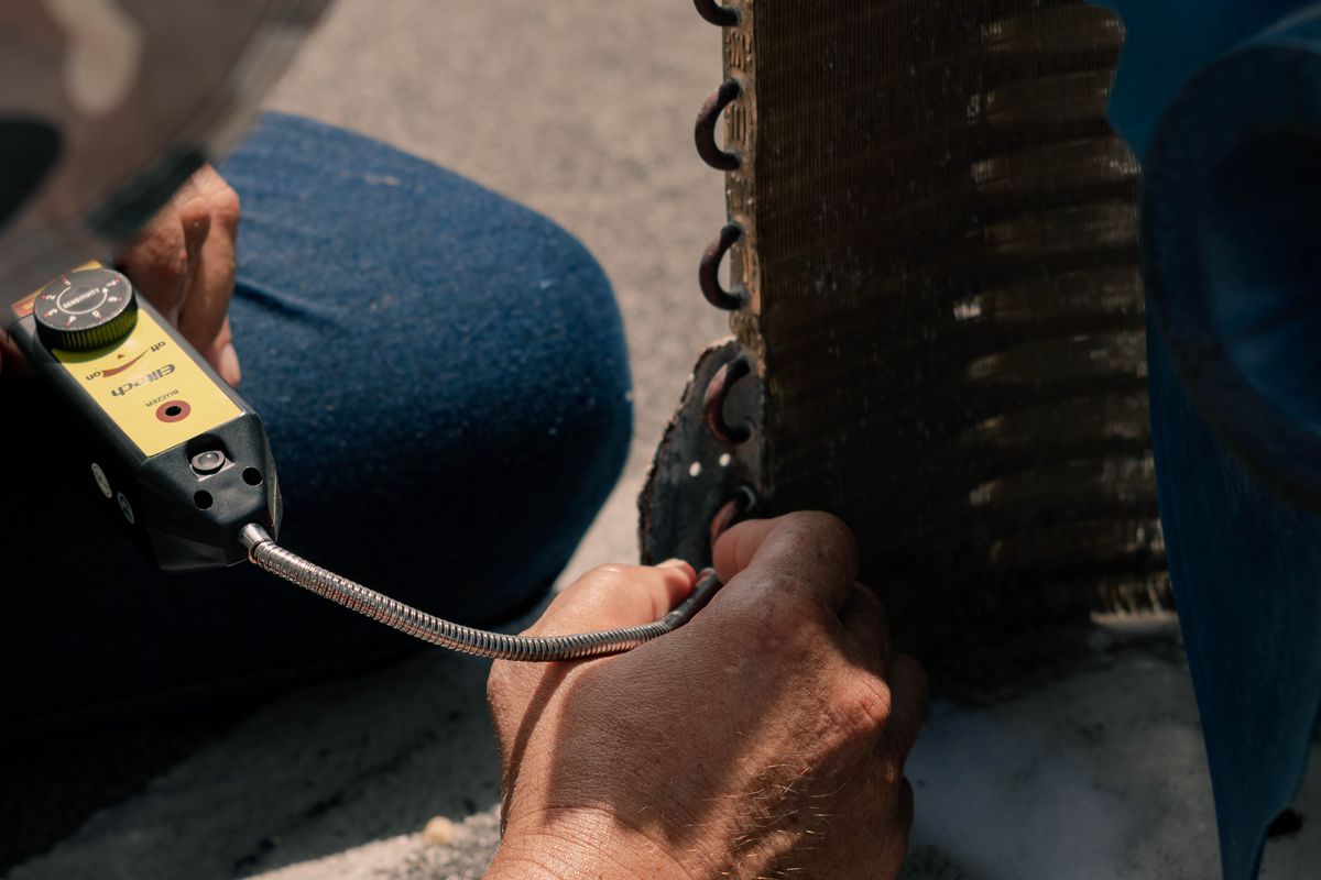HVAC technician working on a failed air conditioner with hand tools during a repair call.
